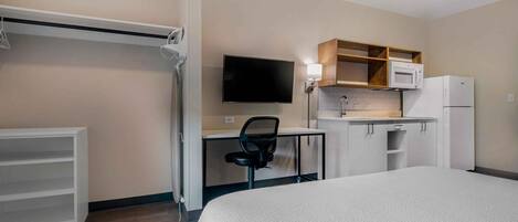 A hotel room with a bed, a desk with a chair, a television, a microwave, and a refrigerator.