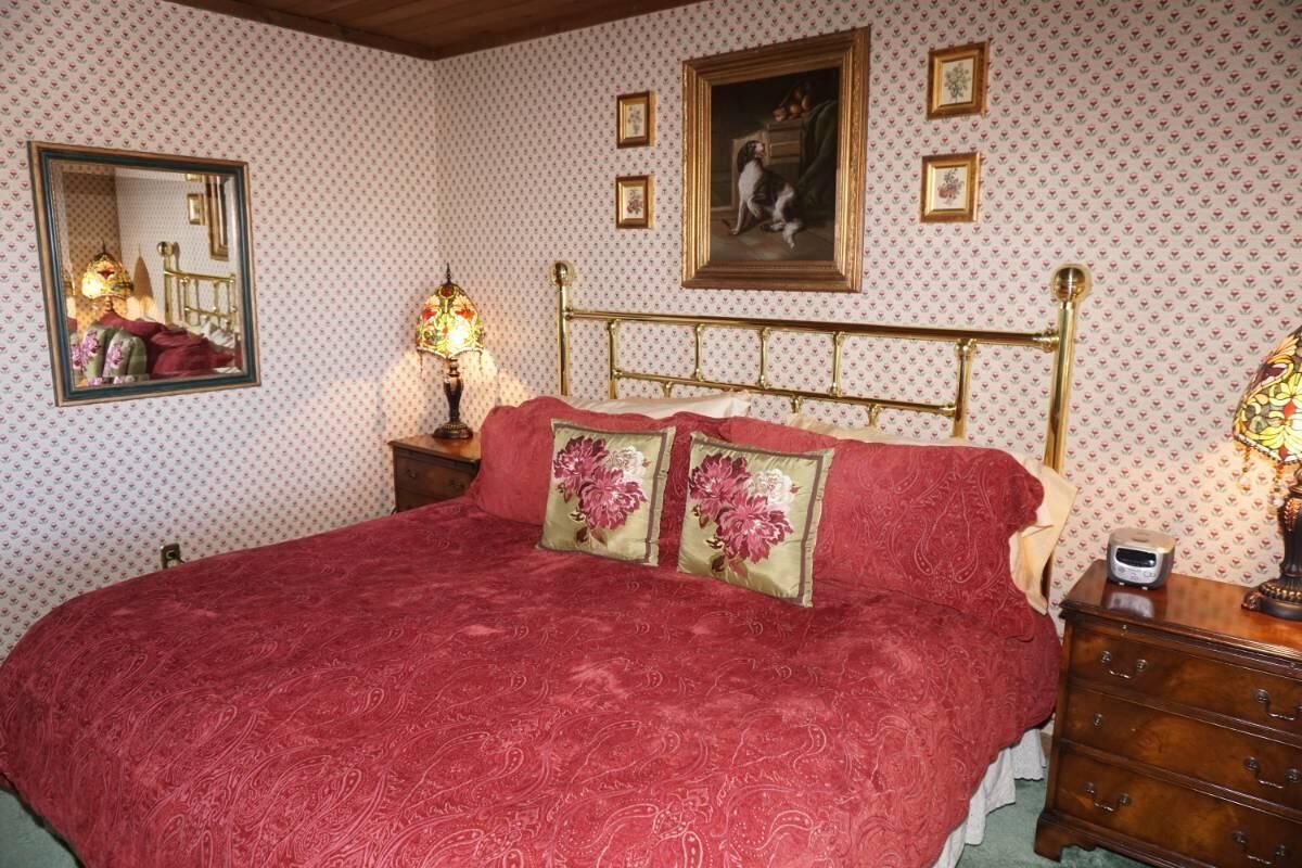 A bedroom with a large bed, a wooden headboard, two bedside tables, a mirror, and a framed picture on the wall.