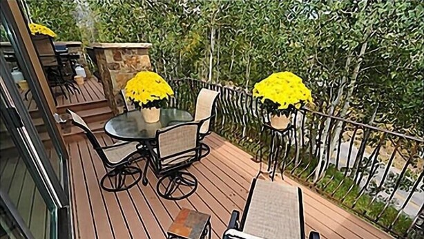 A wooden deck with a glass-top table and chairs, surrounded by a metal railing and greenery. - 35 Alpine Ln (Snowmass Village)