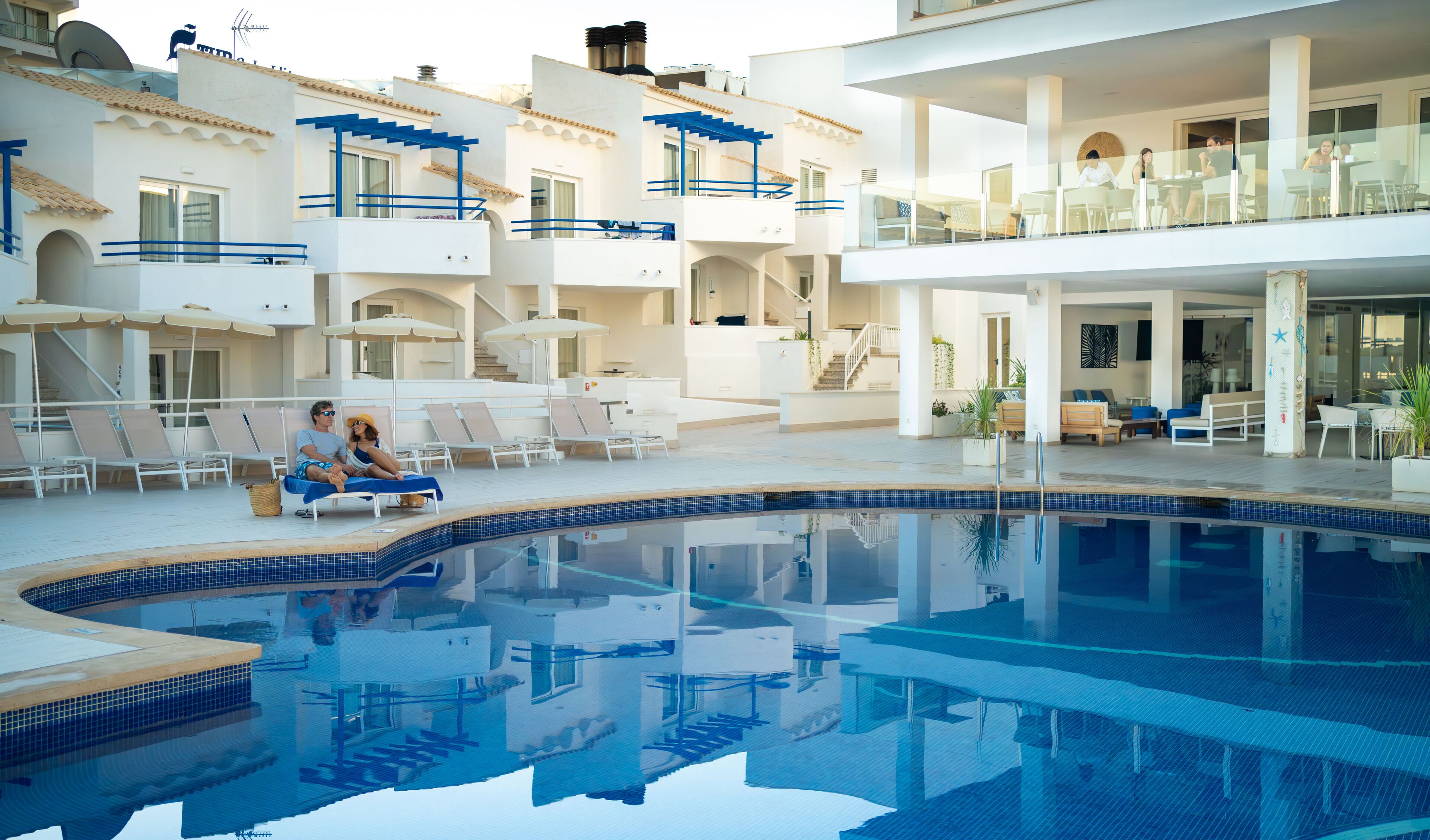 A modern hotel with a swimming pool, lounge chairs, and a dining area with tables and chairs.