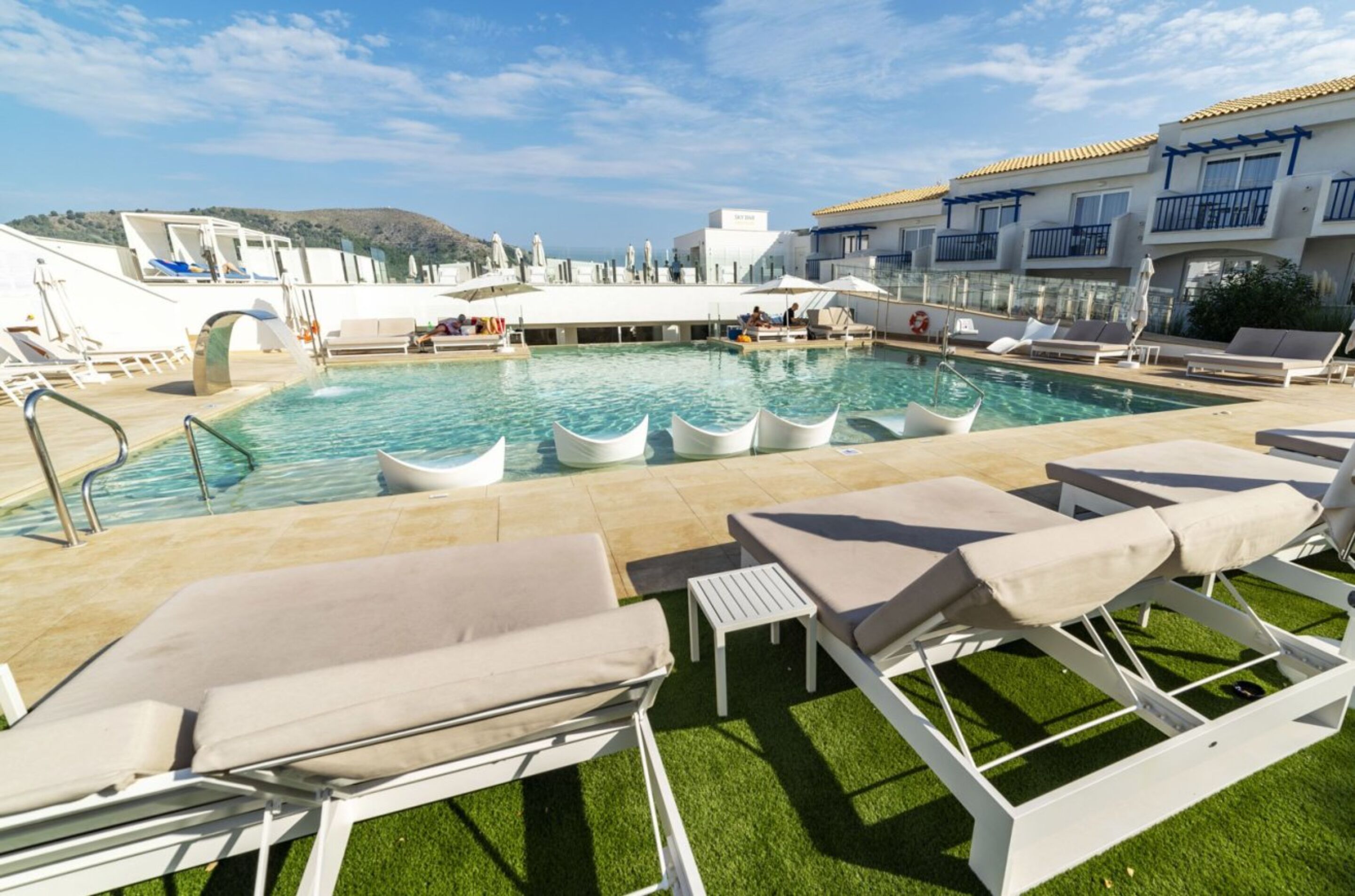 Un área de piscina con tumbonas, piscina y un edificio con balcones.