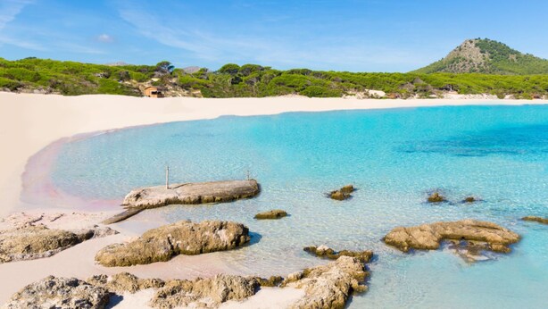 En strand med kristallklart turkosfärgat vatten, vit sand och klippiga utskott.