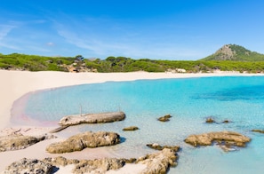 Una playa con agua turquesa cristalina, arena blanca y afloramientos rocosos.