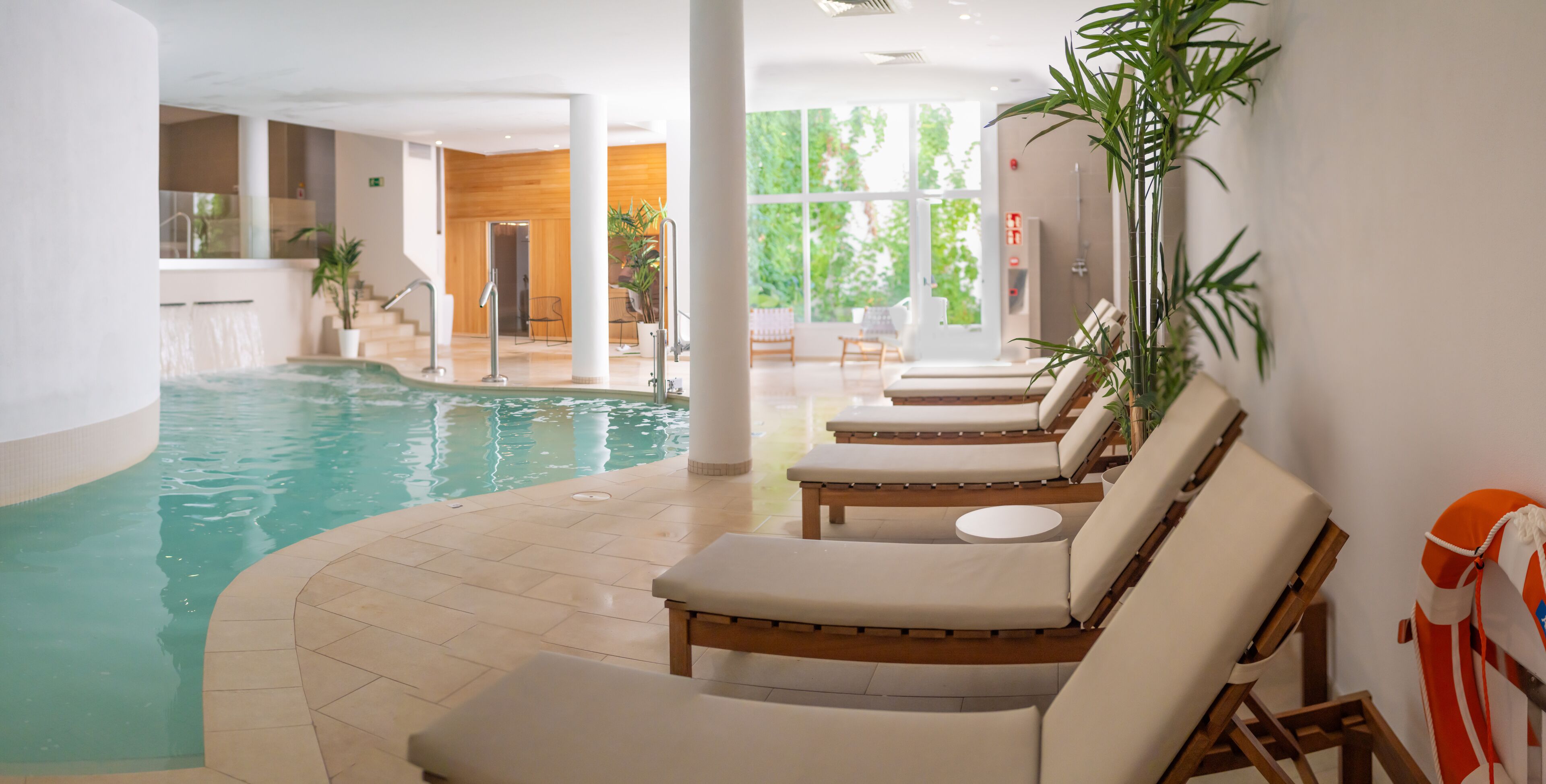 An indoor swimming pool with lounge chairs and potted plants.