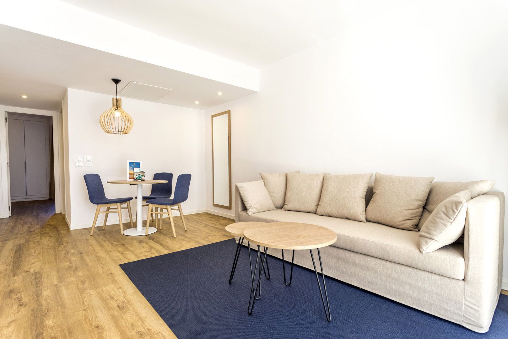A modern living room with a beige sofa, a round coffee table, and two blue chairs around a small table.