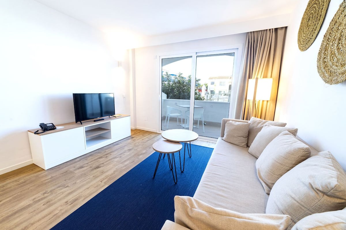 A modern living room with a flat-screen TV, a white entertainment unit, a round coffee table, and a beige sofa.