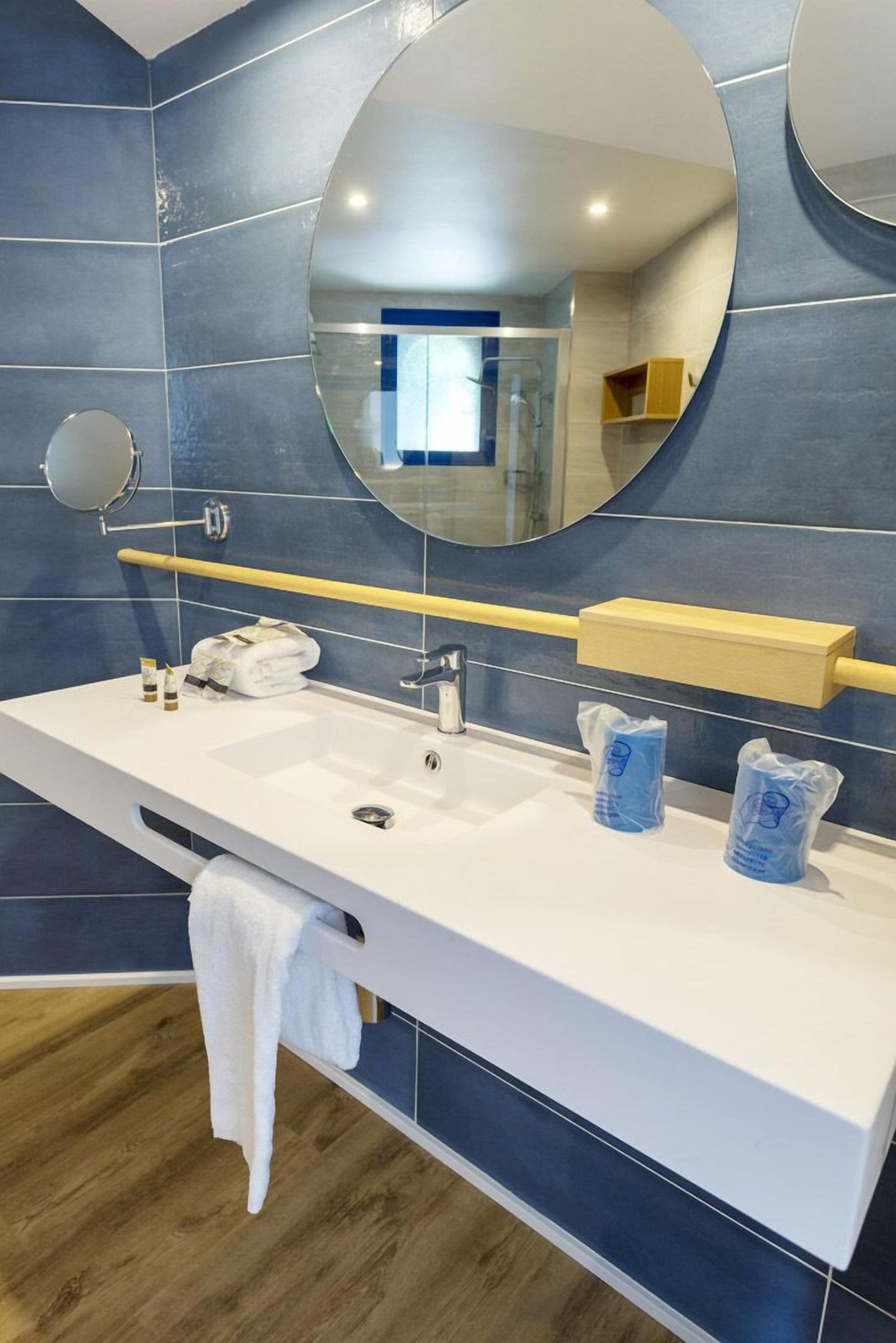 Un baño moderno con un lavamanos blanco, dos espejos y una pared con azulejos azules.