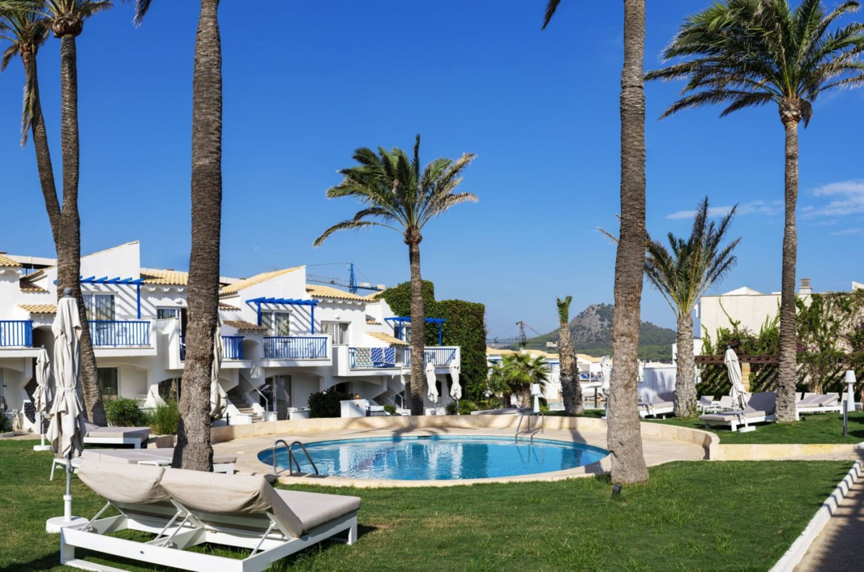 A pool area with lounge chairs, palm trees, and a building with balconies.