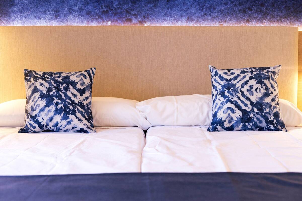 A hotel room with a bed featuring white linens and two matching blue patterned pillows.
