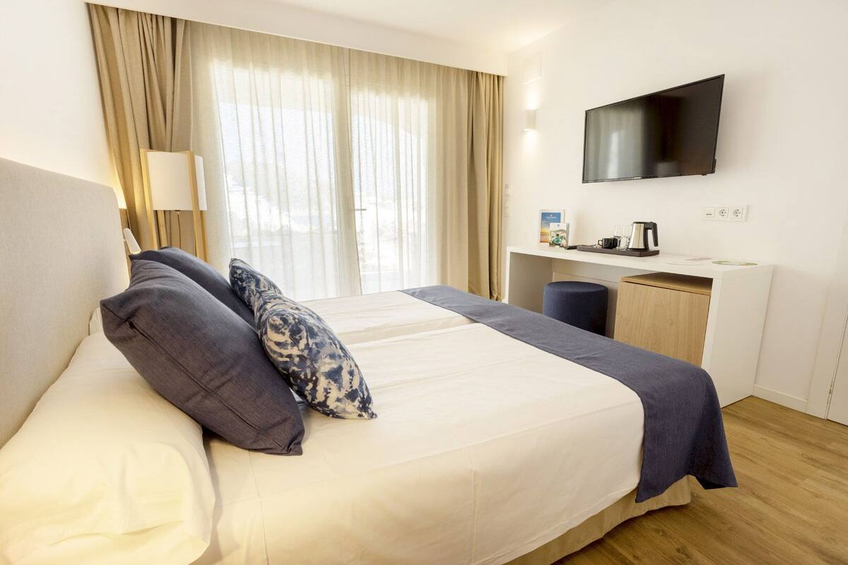 A hotel room with a bed, a desk, a television, and a window with curtains.
