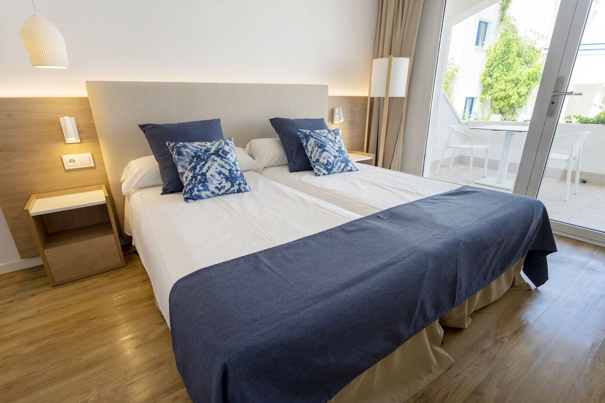 A hotel room with a large bed, two bedside tables, a nightstand, and a view of the outdoors.