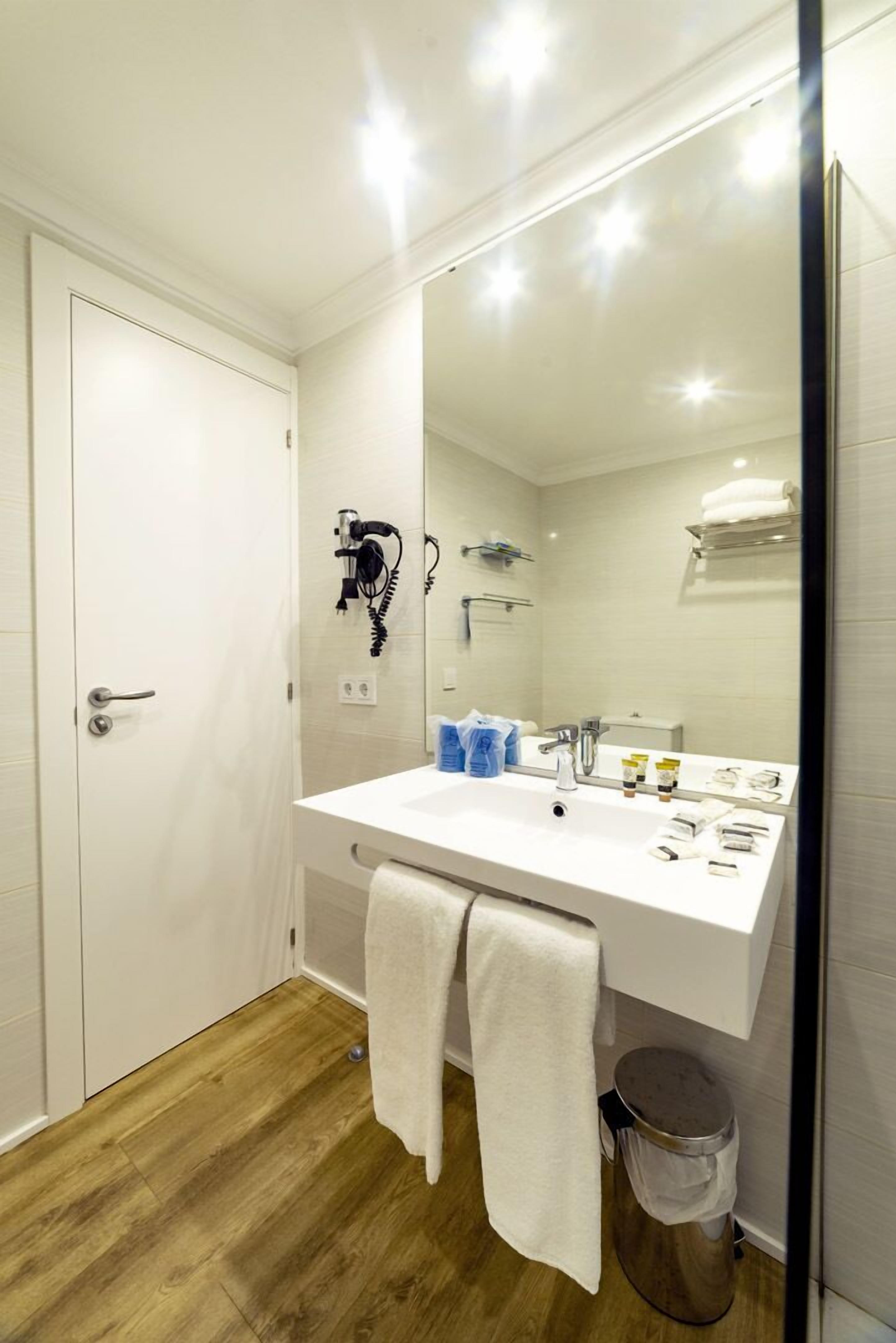 A modern bathroom with a white sink, mirror, and wooden flooring.
