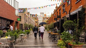 A pedestrian street lined with outdoor seating and potted plants, with people walking and dining. - The Wellington Suite next to Sloane Square (London)