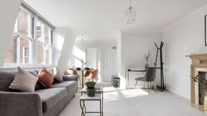 A modern living room with a grey sofa, a small table with a plant, and a fireplace. - The Wellington Suite next to Sloane Square (London)