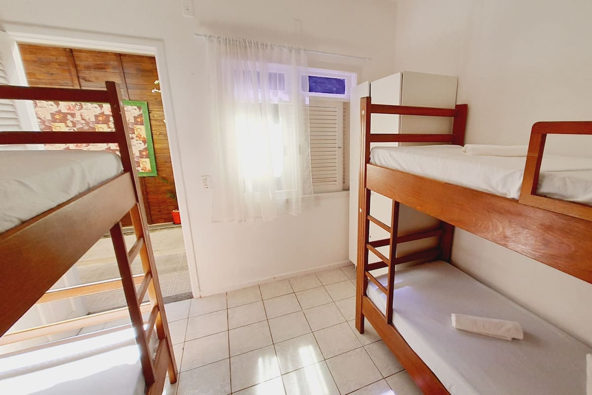 Ein Schlafsaalzimmer mit Etagenbetten, einem kleinen Fenster mit Vorhängen und einem gefliesten Boden.