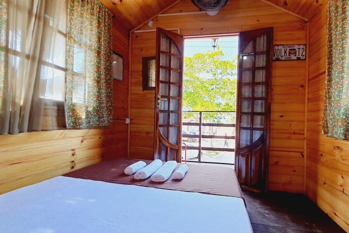 Ein Zimmer in einer Holzhütte mit einem Bett, einem Fenster mit Vorhängen und einem Schild mit der Aufschrift 'Vulk T2'.