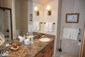 A bathroom with a granite countertop, two sinks, a large mirror, wall-mounted towel racks, and a toilet. - 381 Ridge Rd #C1 (Snowmass Village)