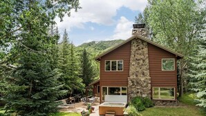 A two-story cabin with a stone chimney, surrounded by dense forest.