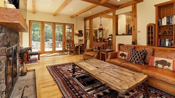 A spacious living room with a stone fireplace, wooden beams, a leather sofa, and a large rug.