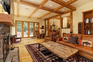 Ein geräumiges Wohnzimmer mit Kamin aus Stein, Holzbalken, einer Ledersofa und einem großen Teppich.