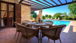 A covered outdoor dining area with wicker chairs and a table, overlooking a swimming pool. - Villa 64 Anarita - Three Bedroom Villa, Sleeps 6 (Kouklia)