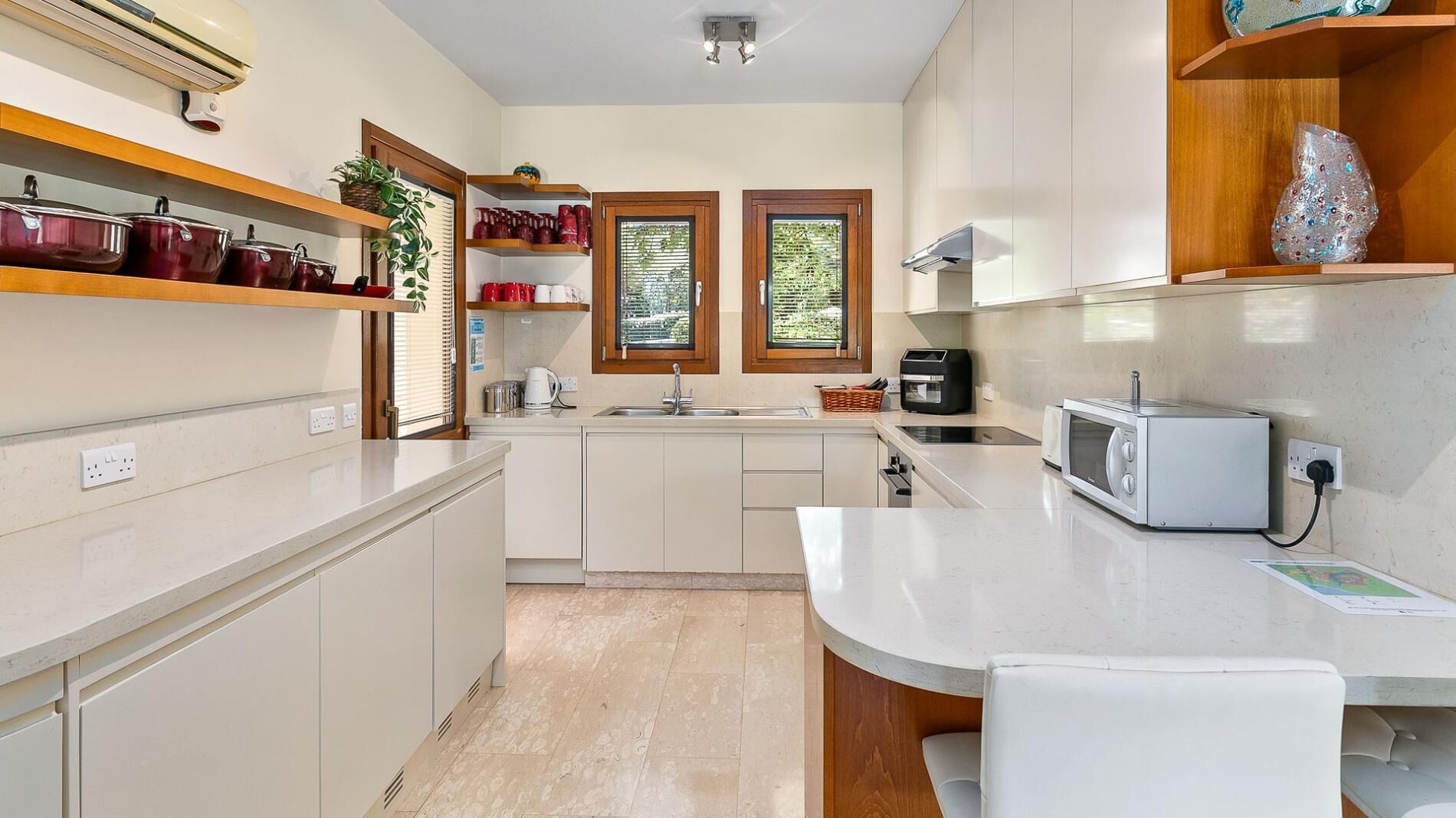 A modern kitchen with white cabinets, a built-in oven, a microwave, and a sink. There are wooden shelves above the counter holding various kitchen items.