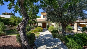 Une villa de style méditerranéen, avec un chemin de pierre menant à l’entrée, entourée d’une végétation luxuriante et d’arbres matures.