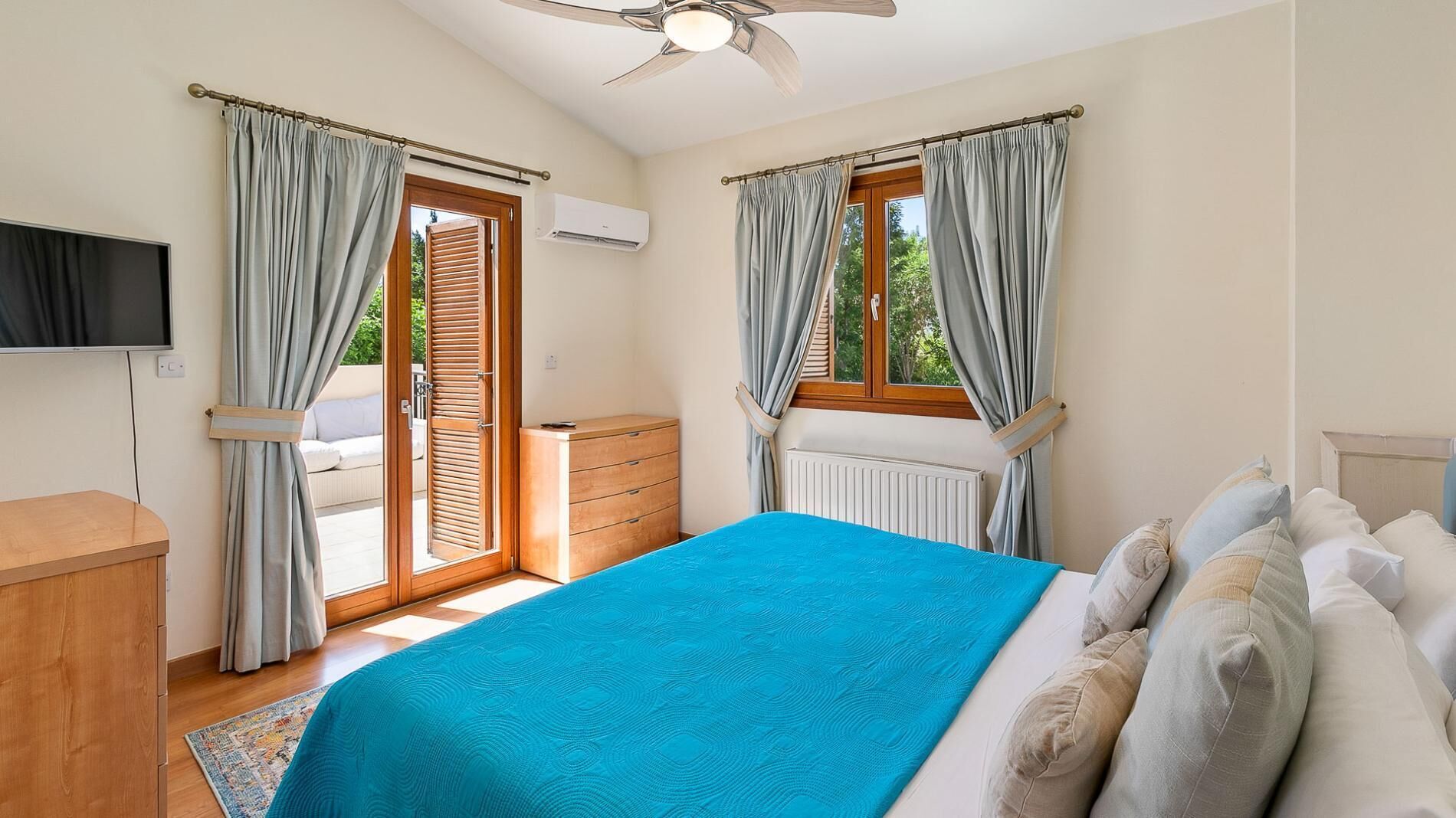 A bedroom with a bed, a wooden dresser, a television, and a window with curtains.