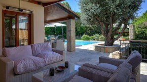 Une terrasse avec des meubles en osier, une piscine et un grand arbre.