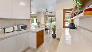 Une cuisine moderne avec des meubles blancs, un four à micro-ondes et un grille-pain. On y trouve un coin repas avec une table et des chaises, ainsi qu'un ventilateur de plafond.