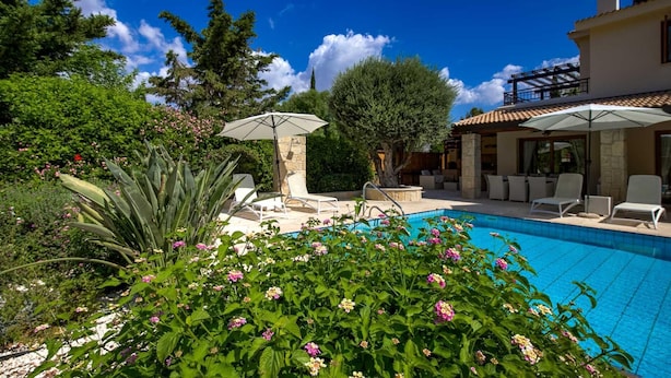 Un espace piscine agrémenté de chaises longues et de parasols, entouré d’une végétation luxuriante et de plantes en fleurs.