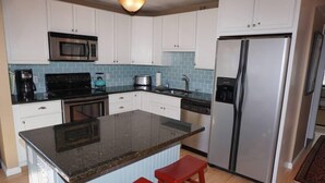 Una cocina con gabinetes blancos, un refrigerador de acero inoxidable, un microondas, una estufa y un lavamanos.
