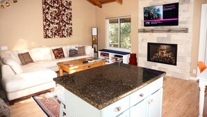 Una sala de estar con chimenea de piedra, un televisor grande montado en la pared y un rincón de estar acogedor con sofá y mesa de centro.