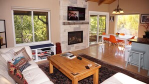 Una sala de estar con chimenea de piedra, una mesa de centro de madera y un ventanal con vistas a árboles.