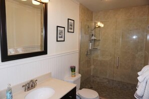 A bathroom with a large mirror, a sink, a toilet, and a glass-enclosed shower.