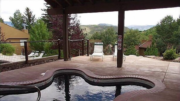Una piscina de diseño curvo, rodeada por un patio cubierto con sillas y vistas a colinas.