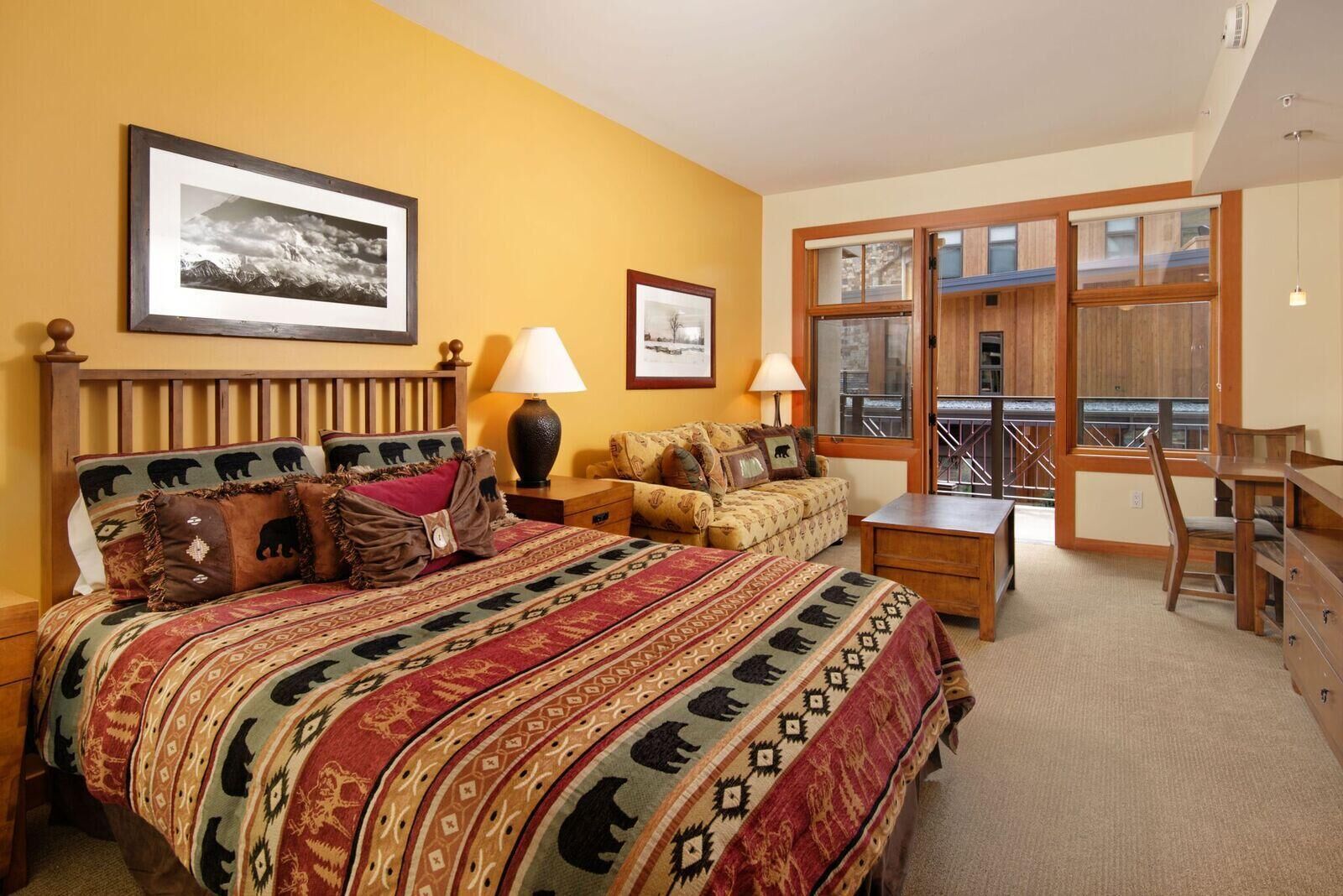 Een slaapkamer met een groot bed, twee nachtkastjes, een bank, een bureau en een raam met balkon.