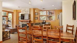 Une cuisine spacieuse avec une grande table à manger et des chaises en bois, une cheminée en pierre et un téléviseur fixé au-dessus.