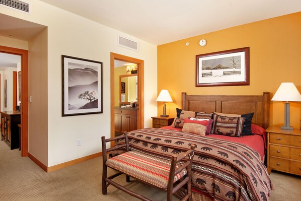 A bedroom with a large bed, two bedside lamps, a wooden headboard, and a framed picture on the wall.