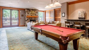 Une table de billard dans une pièce dotée d’une cheminée en pierre, d’un canapé et offrant une vue sur l’extérieur.