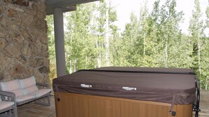 Ein Whirlpool mit Holzverkleidung und braunem Deckel, auf einer Holzterrasse mit einer Steinmauer und einer Bank im Hintergrund.