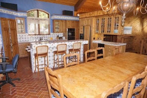 A spacious kitchen with wooden cabinets, a large island with bar stools, and a dining table with chairs. - 201 Edgewood Ln (Snowmass Village)