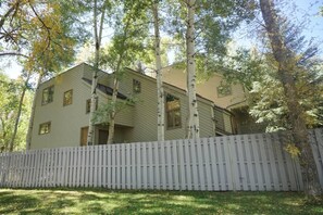 A two-story house with a white picket fence, surrounded by trees. - 735 Bleeker St E #735 (Aspen)