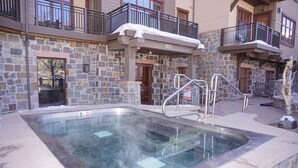 A spa area with a hot tub, stone walls, and a balcony with a railing.