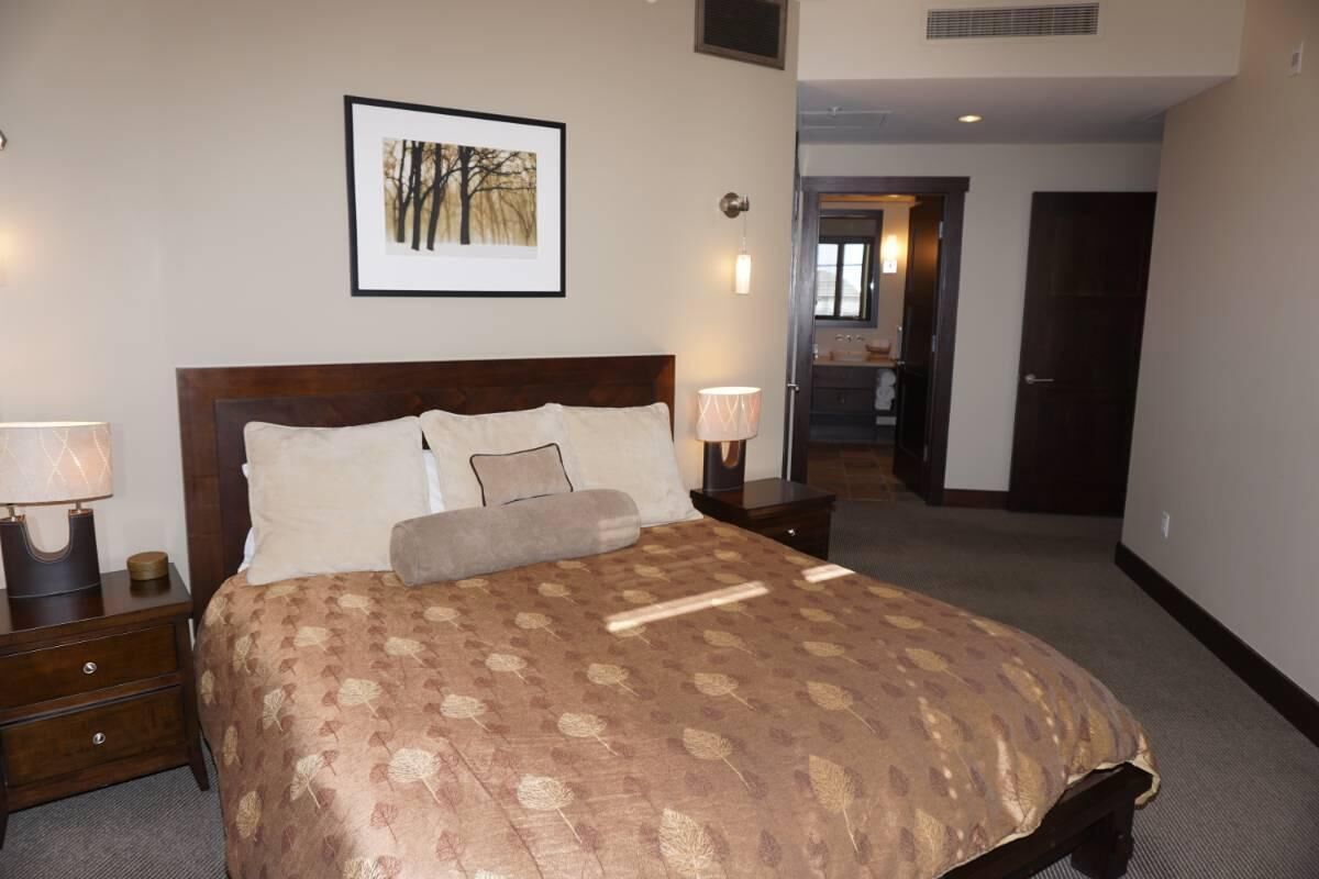 A neatly made bed with a patterned bedspread, a framed picture on the wall, and two bedside lamps.
