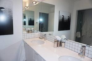 A modern bathroom with two sinks, a large mirror, and a towel rack.