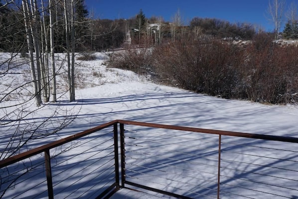A snow-covered outdoor area with a metal railing, bare trees, and a distant building.