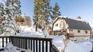 A snow-covered residential area with a wooden deck and a house with a sloped roof.