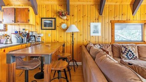 A cozy cabin interior with a wooden dining area, bar stools, a sofa, and a large window.