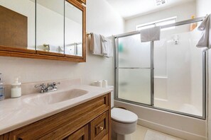 Ein Badezimmer mit einem Holzlagerfläschchen, einem weißen Waschbecken, einem Spiegel, einer Toilette und einer Duschkabine.